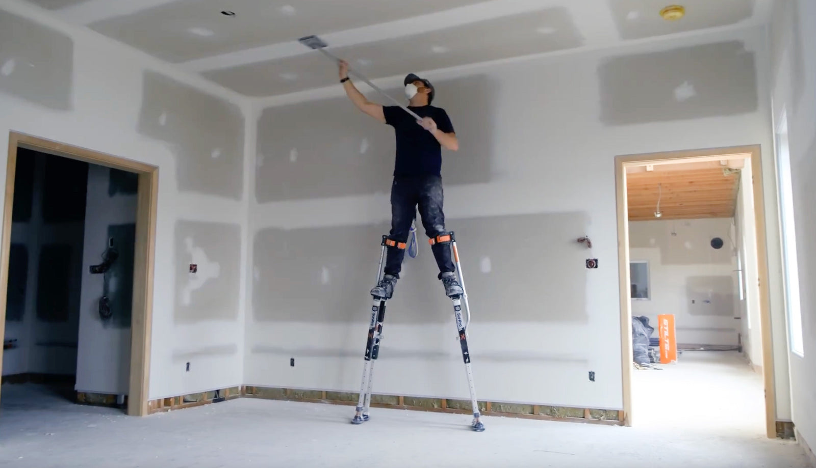 A drywaller sanding a ceiling while on drywall stilts